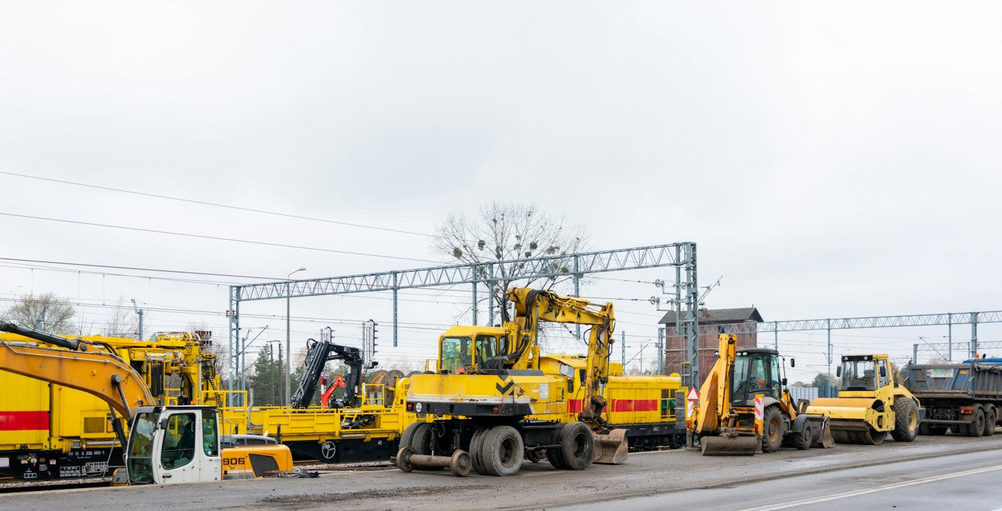Construction vehicles parked by a railway line on an overcast day.