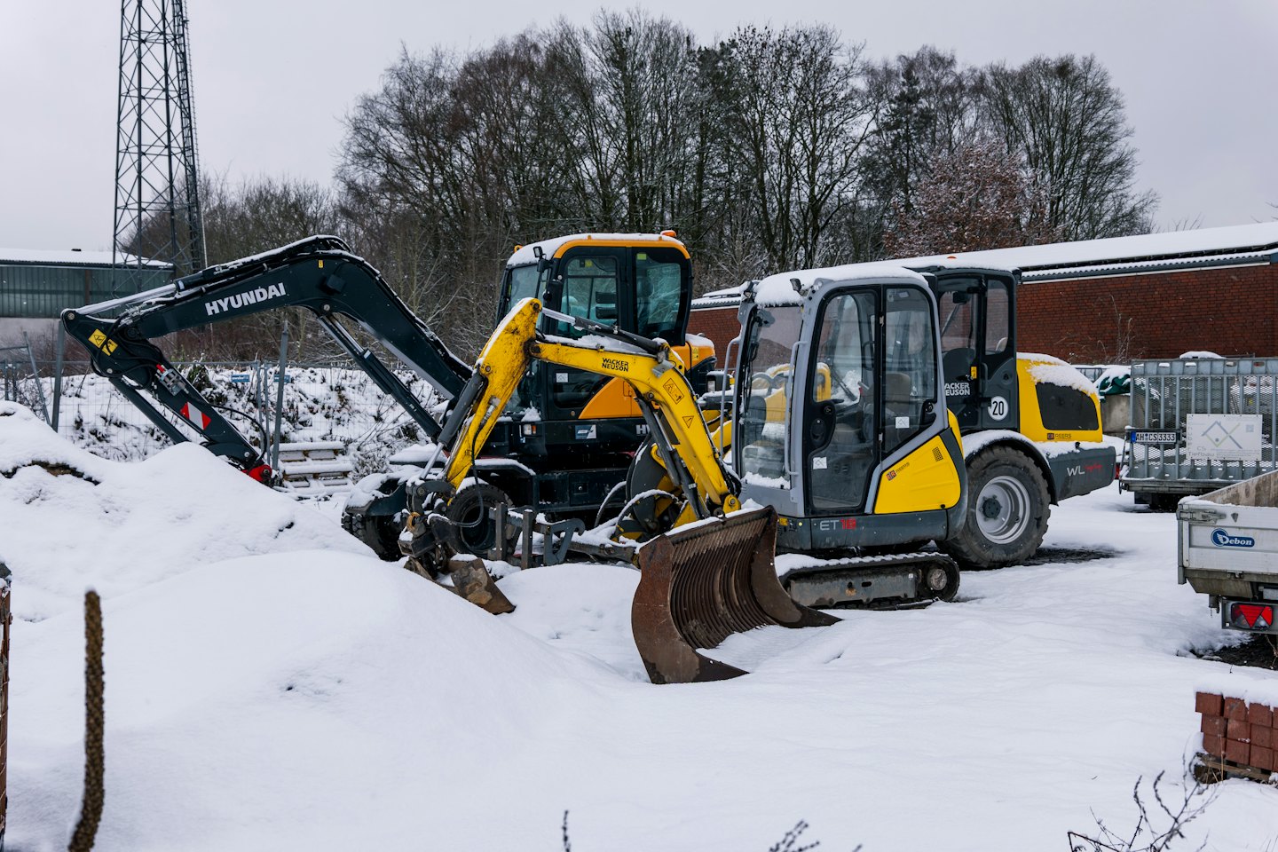 Snow covered construction vehicles parked in a quiet depot.