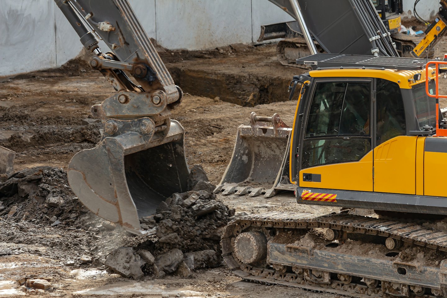 Yellow excavator bucket digging brown earth on construction site.